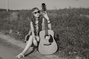 Hippie girl travelling with her guitar on a road