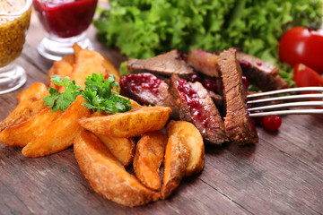 Beef with cranberry sauce, roasted potato slices on cutting board, on wooden background