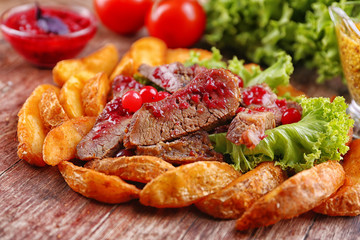 Beef with cranberry sauce, roasted potato slices and bun on wooden cutting board, close-up