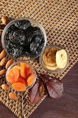 Prunes and other dried fruits with grape leaves on wicker mat, closeup