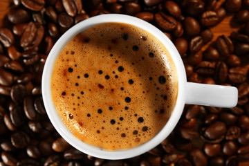 Cup of fresh coffee with beans on table, closeup