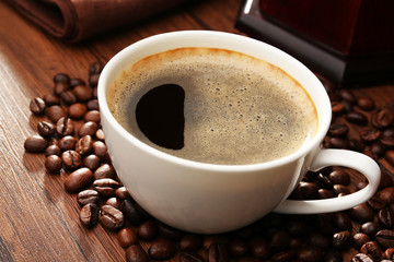 Cup of fresh coffee with beans on table, closeup