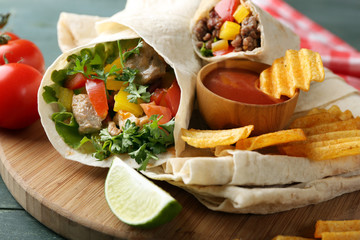 Homemade tasty burrito with vegetables, potato chips on cutting board, on wooden background