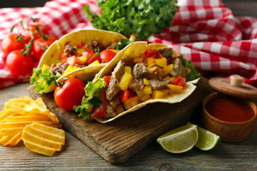 Homemade tasty burrito with vegetables and potato chips on cutting board, on wooden background