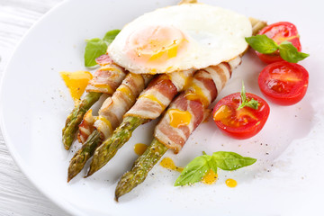 Dish of asparagus with bacon and egg in plate on table, closeup
