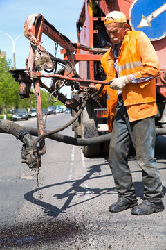 Construction worker during patch pothole repairing works on road