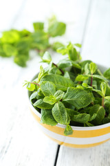 Fresh mint in bowl on white wooden background