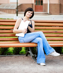 Fototapeta premium brunette girl sitting on a sunny day on a bench in the park with
