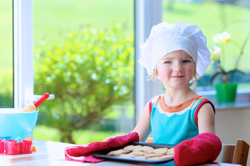Little happy child, adorable toddler girl wearing white chef hat and red gloves helping mother...