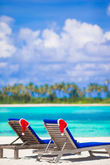 Two loungers with red Santa hats on tropical beach with white