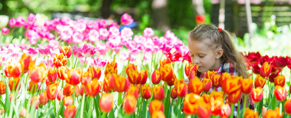 Little adorable girl smelling colorful tulips at summer garden