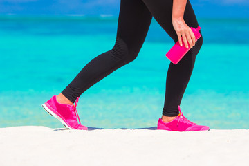 Closeup of female legs in sneakers running on white sandy beach