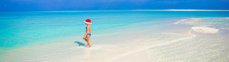 Fototapeta na wymiar Little girl in Santa hat on the beach during vacation