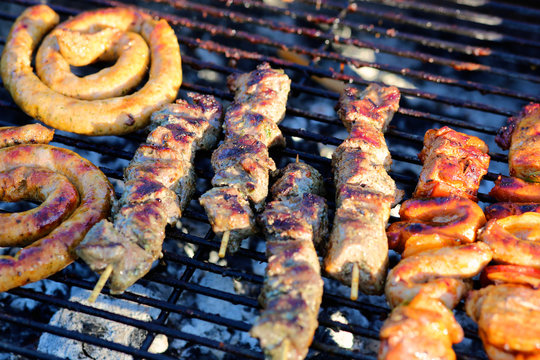 Assorted mixed grill on wooden skewers from chicken meat, lamb and pork, sausages and various vegetables roasting on barbecue grid cooked for summer family dinner