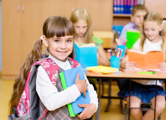 portrait of pretty preschool girl with books in classroom