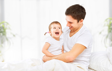 Happy family father and baby  daughter playing in bed