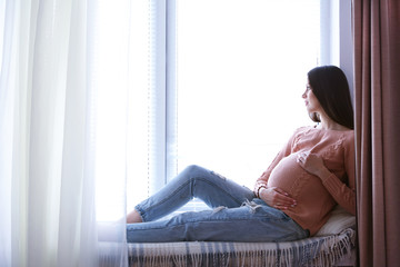 Pregnant woman sitting on windowsill background