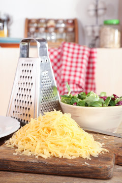 Grated cheese on wooden table in kitchen, closeup