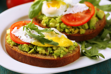 Tasty sandwiches with egg, avocado and vegetables on plate, on wooden background