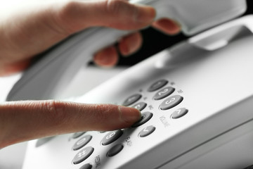 Finger pressing number button on telephone to make a call, close up