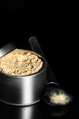 Jar with loose cosmetic powder and makeup brush, isolated on black