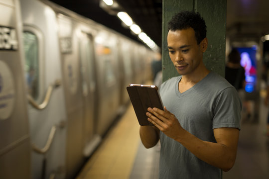 Young African Asian Man In Subway Using Tablet Pc