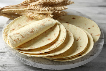 Stack of homemade whole wheat flour tortilla on cutting board, on wooden table background