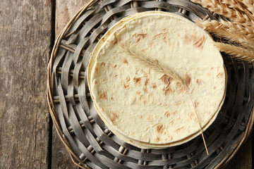 Stack of homemade whole wheat flour tortilla on wicker mat, on wooden background