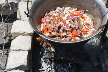 Hungarian taditional cauldron with beef stew cooking on fire outdoors 