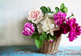 Basket with peonies and roses on an old wooden table