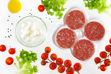 raw burger meat with food ingredients: tomatoes cherry, olive, o