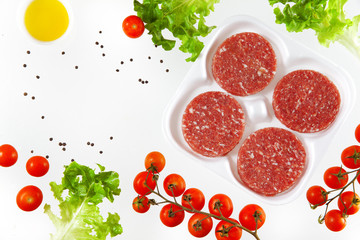 raw burger meat with food ingredients: tomatoes cherry, olive, o