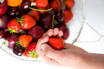 Hand holding Strawberry above Summer Berries and Fruits in the b