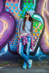 beautiful cool girl in hat and sunglasses over graffiti wall