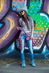 beautiful cool girl in hat and sunglasses over graffiti wall