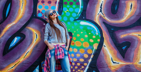 beautiful cool girl in hat and sunglasses over graffiti wall
