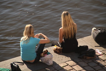 Mujeres jóvenes sentadas en la ribera del río Vtlava en Praga en un día de verano