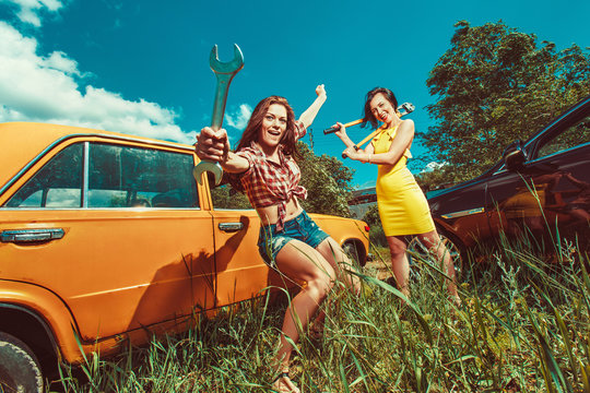 Cheerful woman mecanic is repairing a car with the wrench anothe
