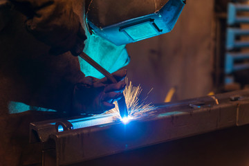 Young man with protective mask welding in a factory