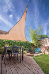 Modern house terrace in summer with table and shade sail, outdoor home living space