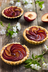 Tartlets with plum on wooden background