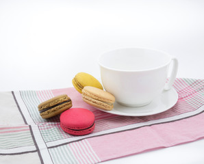 Colorful macarons with white cup and plate on pink cloth.
