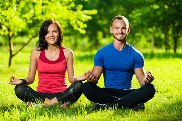 Young man and woman doing yoga in the sunny summer park