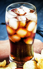 Potato chips and cola with ice in a large glass, selective focus