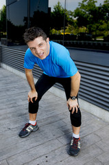 Fototapeta premium young attractive man leaning exhausted after running session sweating taking a break to recover in urban street