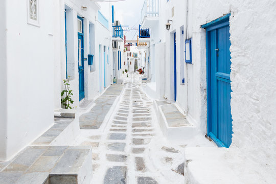 Mykonos, Greece - Traditional whitewashed street of Mykonos town with blue windows and doors on a sunny summer morning. Empty alleyway at sunrise © zgphotography
