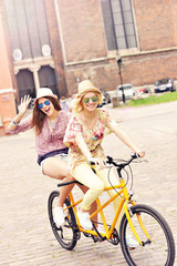 Two happy girl friends riding tandem bicycle