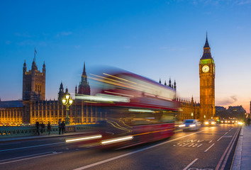 London, United Kingdom - Iconic Double Decker bus on the move on Westminster bridge with illuminated Big Ben clock tower and Parliament at background at blue hour