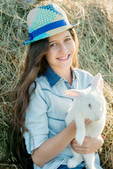 cute teen girl with white rabbit sitting in front of haystack