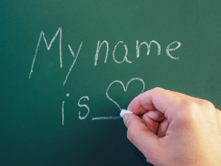 Person writing on green chalkboard with calk
